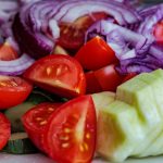 Colorful summer vegetable salad featuring tomatoes, cucumbers, and red onion slices on a plate.